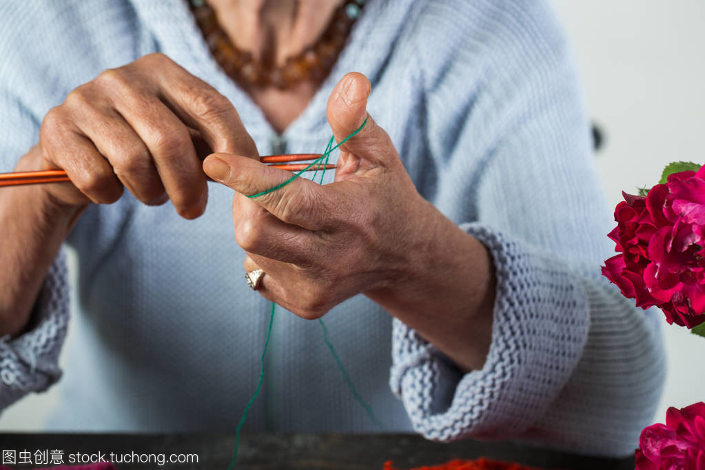 奶奶织羊毛线程和织针、 羊毛过冬。手工制作。老女人编织,美丽的祖母,在蓝色的贴心小棉袄针织羊毛产品,年老时用鲜花的爱好